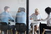 a group of people sitting at a desk watch as a woman writes on a paper